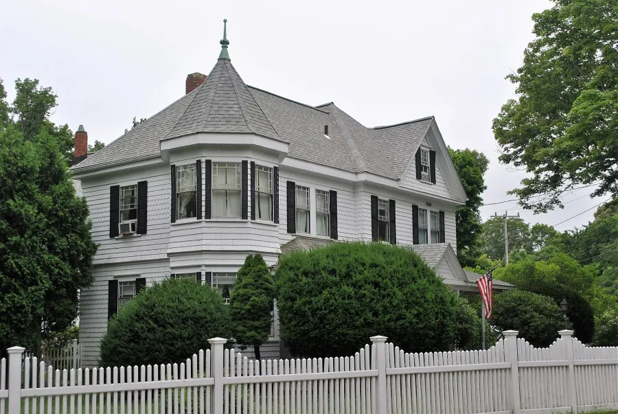 Gray Queen Anne style house behind a white picket fence in Falmouth